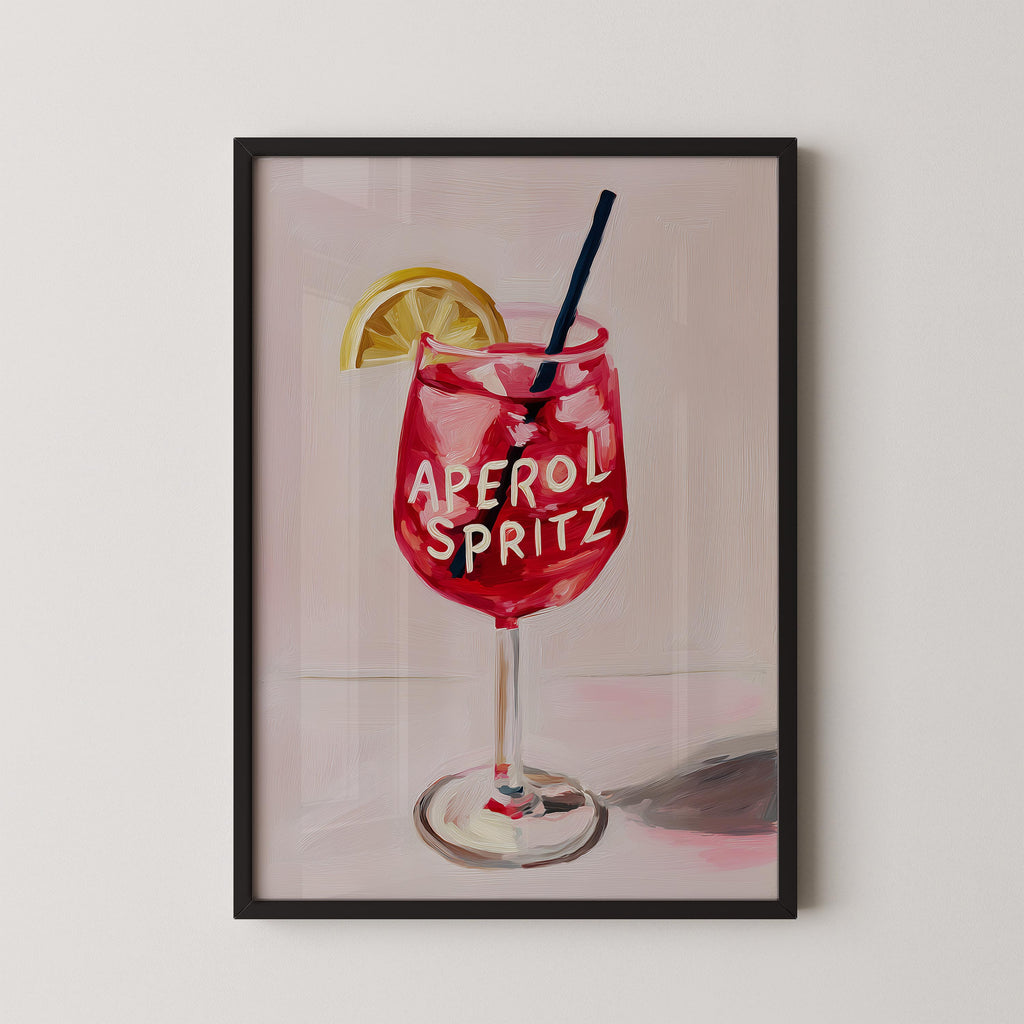 A framed illustration of a red drink with the text "Aperol Spritz" on it, accompanied by a lemon slice.
