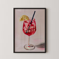 A framed illustration of a red drink with the text "Aperol Spritz" on it, accompanied by a lemon slice.