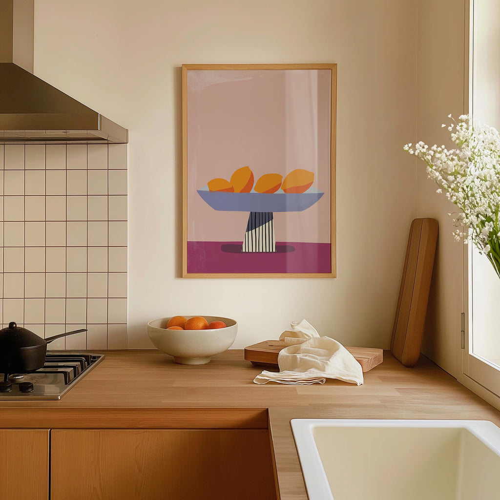 a kitchen counter with a bowl of oranges, a vase of white flowers, and a framed artwork depicting a still life of fruit on a table.