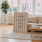 a large framed sign with the text "HOW LUCKY ARE WE" in a living room setting.
