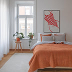 a cozy bedroom with a large bed, a wooden stool with a potted plant, and a large window with white curtains. The room has a warm, inviting atmosphere with the orange bedspread and striped pillows.