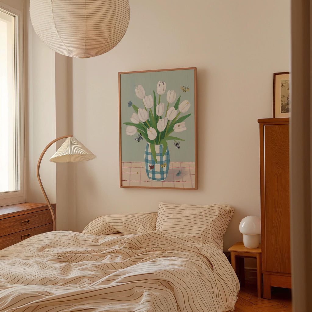 a cozy bedroom with a bed, a lamp, and a painting of a vase of white tulips on the wall.