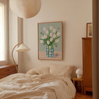 a cozy bedroom with a bed, a lamp, and a painting of a vase of white tulips on the wall.