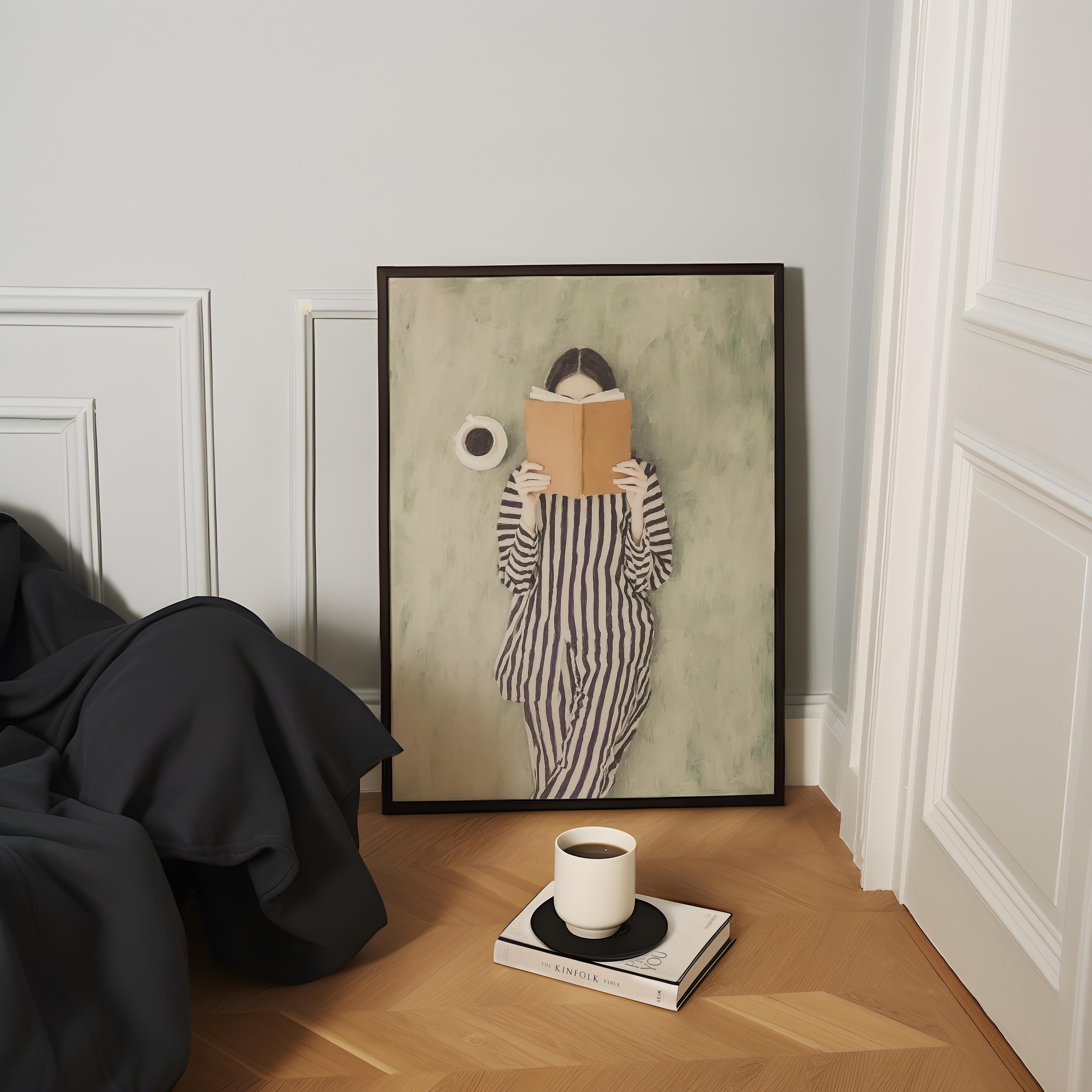 a cozy corner with a framed painting of a person reading a book, a cup of coffee, and a stack of books on the floor.