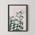 A framed illustration depicting a hand pouring coffee from a coffee pot into two cups on a checkered tablecloth.