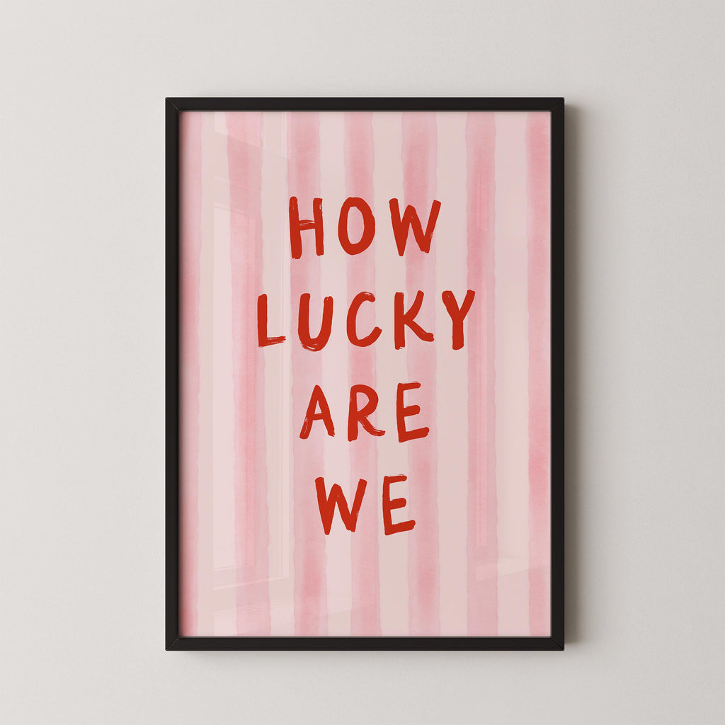 a framed poster with the text "HOW LUCKY ARE WE" written in bold red letters against a pink striped background.