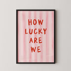 a framed poster with the text "HOW LUCKY ARE WE" written in bold red letters against a pink striped background.