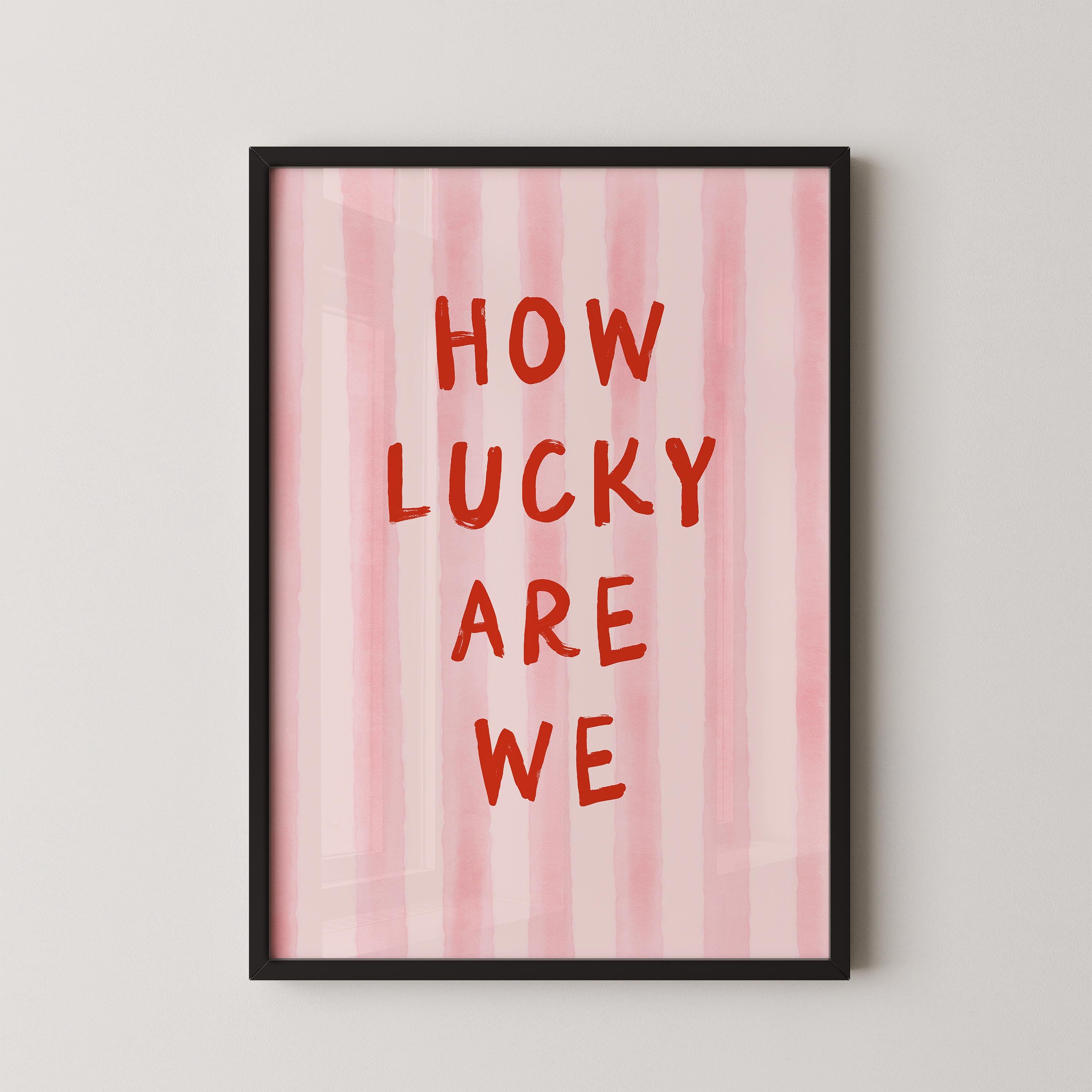 a framed poster with the text "HOW LUCKY ARE WE" written in bold red letters against a pink striped background.