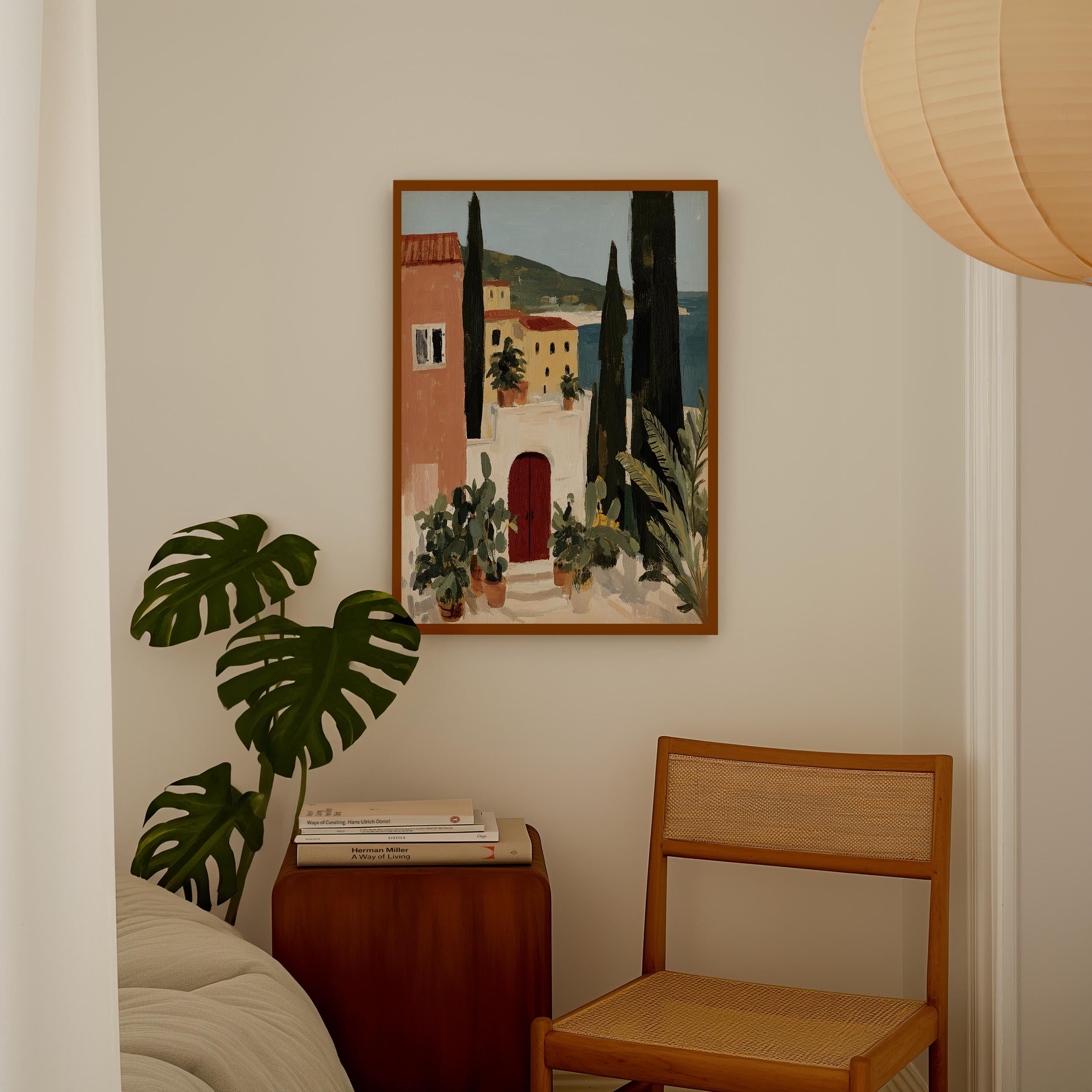 a cozy corner of a room with a painting of a coastal town hanging on the wall, a wooden chair, a stack of books, and a potted plant.