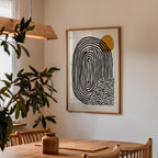 a wooden dining table with a woven placemat, a potted plant, and a framed abstract art piece hanging on the wall above the table.