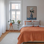 a cozy bedroom with a large bed, a wooden stool with a potted plant, and a painting of a flower on the wall.