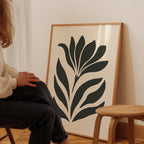 A person is sitting in a chair in front of a large framed artwork depicting a stylized flower or plant design.