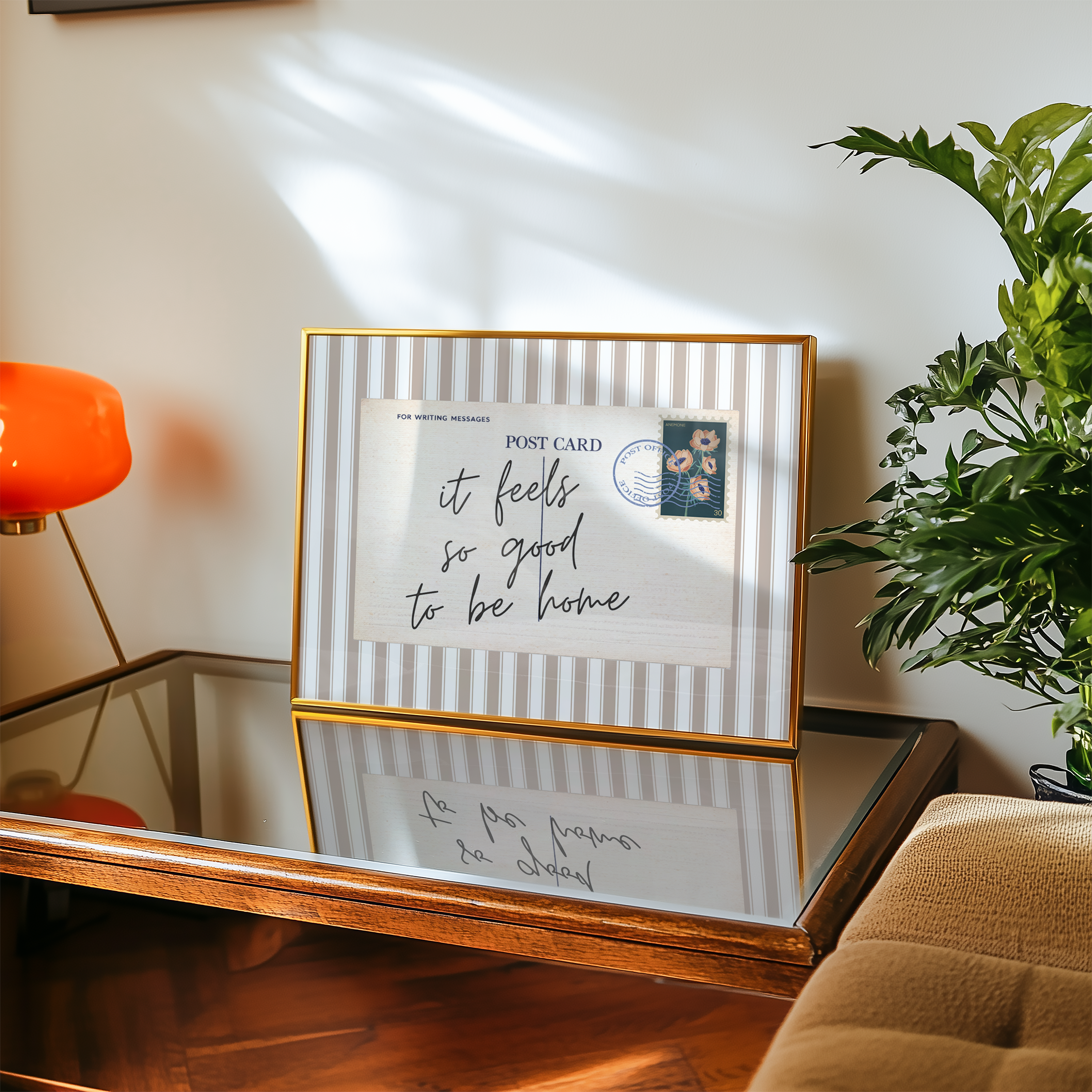a framed postcard with a handwritten message, placed on a wooden table next to a potted plant.