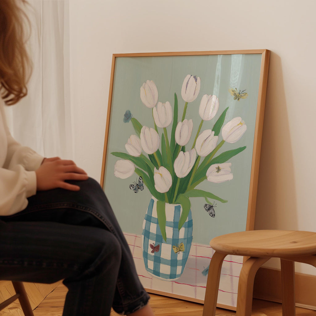 A person is sitting in front of a framed painting of a vase with white tulips and butterflies.