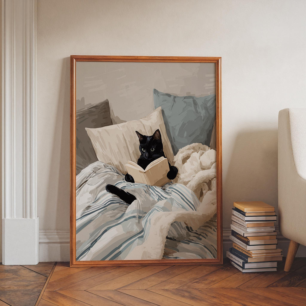 A framed illustration of a black cat lying on a bed and reading a book.