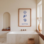 a bathroom with a white bathtub, a framed artwork with seashells and the words "sun & sea" above it, and a window with a vase of flowers.