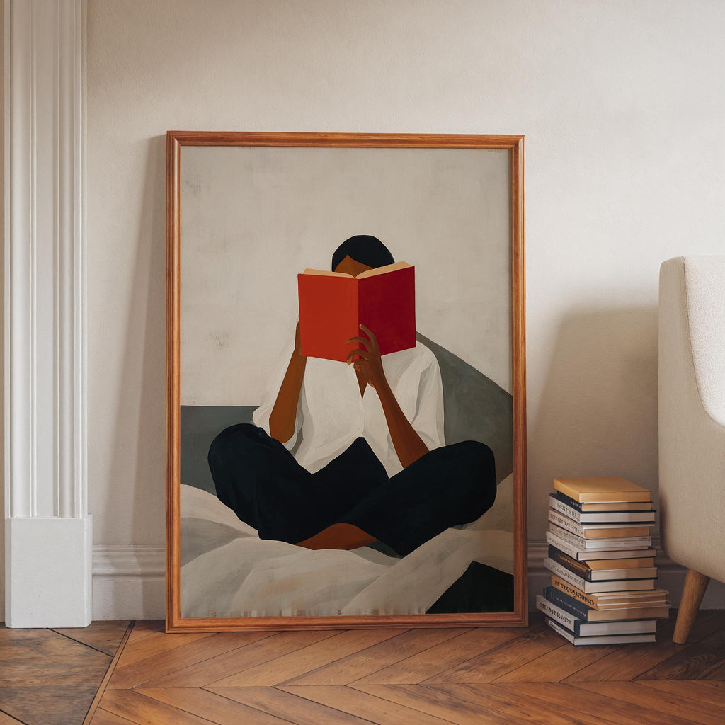 A framed painting depicting a person sitting cross-legged on a bed, reading a red book.