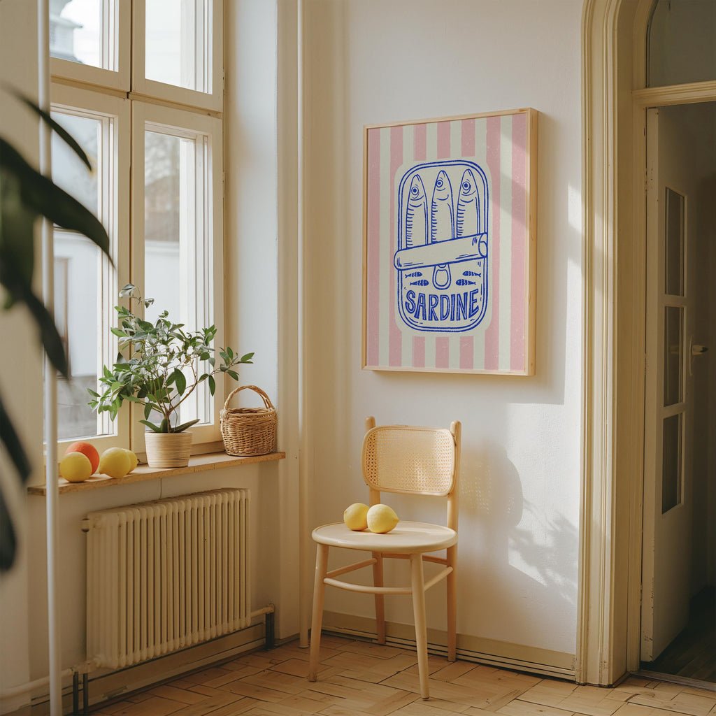 a cozy corner of a room with a wooden chair, a basket of fruit, and a framed poster of a can of Sardine.