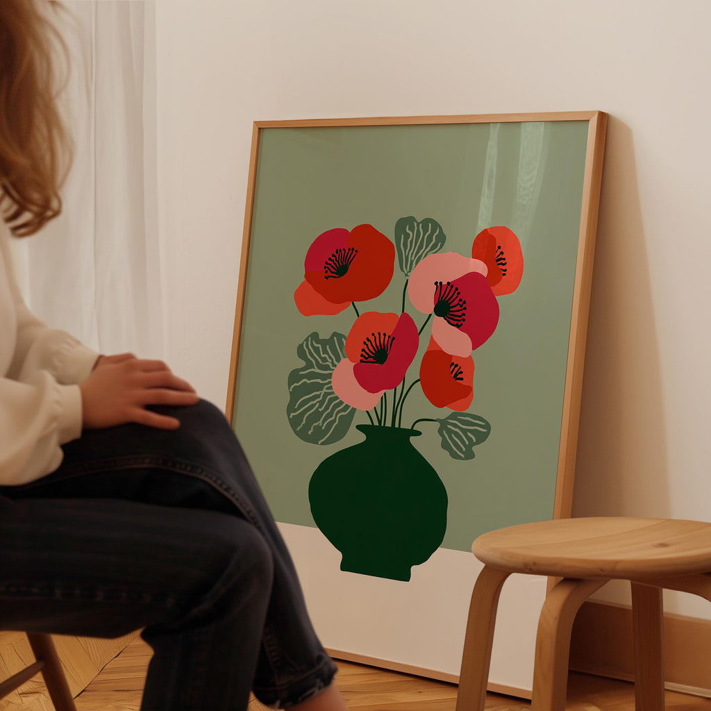 A person is sitting in front of a framed poster featuring a vase with red and pink flowers on a green background.