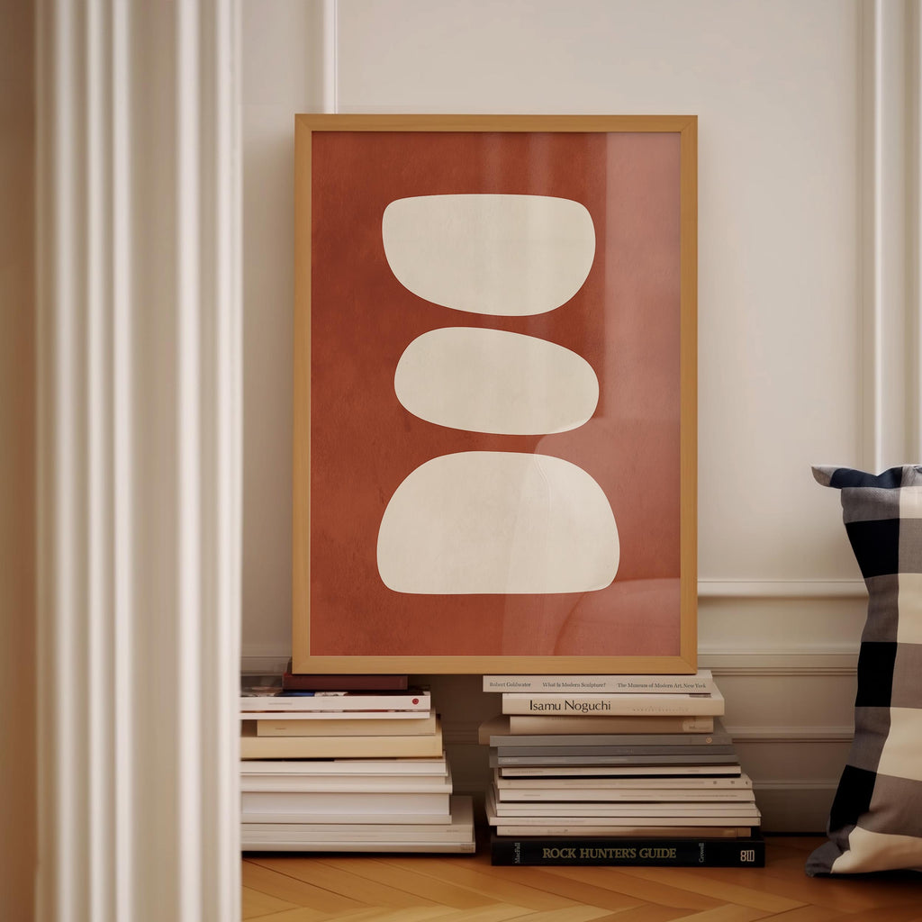 a framed artwork with a bold red background and three white circles, placed on a shelf next to a stack of books.