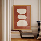 a framed artwork with a bold red background and three white circles, placed on a shelf next to a stack of books.