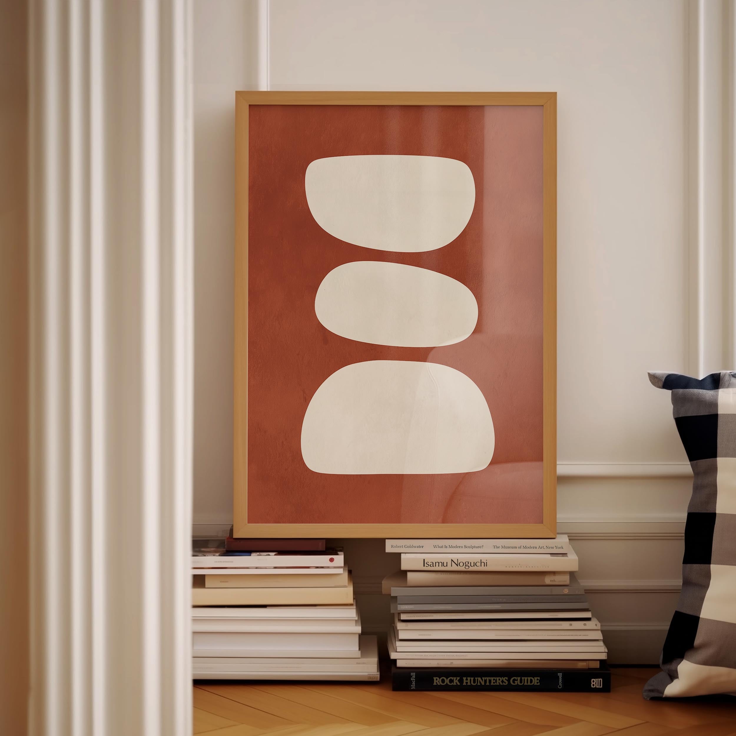 a framed artwork with a bold red background and three white circles, placed on a shelf next to a stack of books.