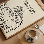 A framed illustration of a table with a vase of flowers, accompanied by the text "GOOD FOOD GOOD MIND" on a wooden surface.