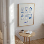 a cozy corner of a room with a wooden table, a white mug, and an open book, along with a framed poster of coffee-making illustrations on the wall.