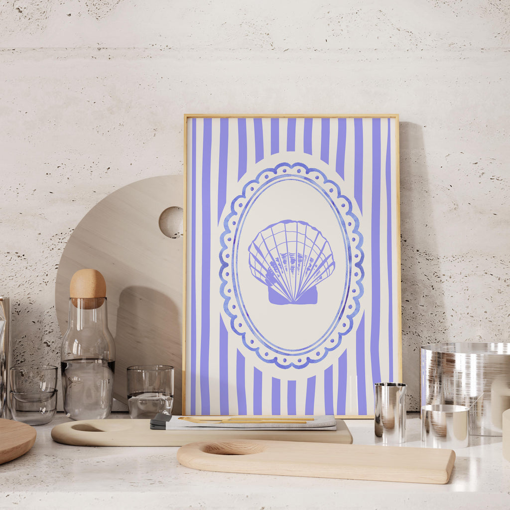 a framed picture of a seashell on a white and blue striped background, placed on a wooden surface.