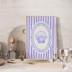 a framed picture of a seashell on a white and blue striped background, placed on a wooden surface.