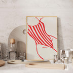 a framed artwork of a red and white striped swimsuit, displayed on a shelf alongside various kitchen items such as a glass bottle, a wooden cutting board, and a metal container.