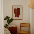 a cozy corner of a room with a framed abstract artwork hanging on the wall, a wooden chair, a small table with books, and a large monstera plant.