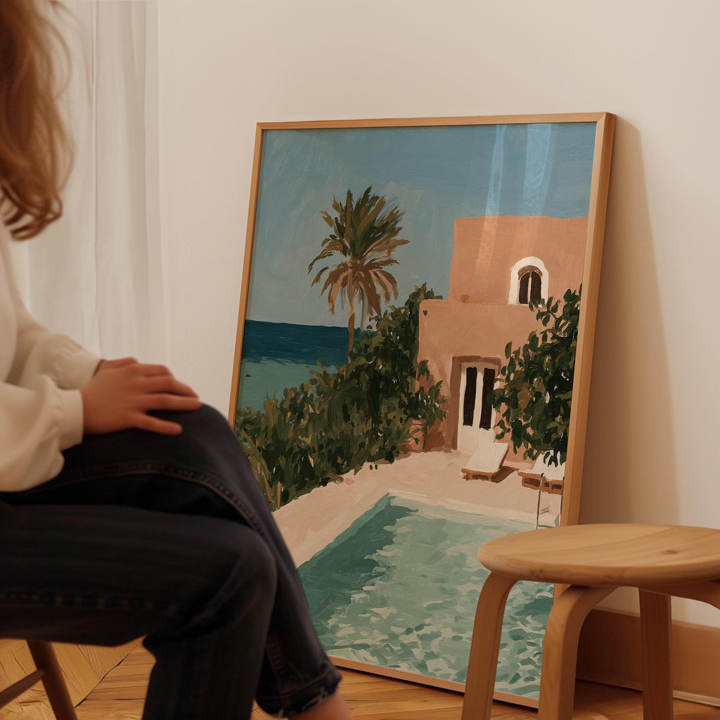 A person is sitting in front of a large painting depicting a tropical beach scene with a pool and palm trees.