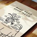 a close-up view of a white paper with a black and white illustration of a table with a vase of flowers and a wine glass. The text "GOOD FOOD GOOD MOOD" is written above the illustration.