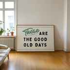 A large framed sign with the text "These are the good old days" is displayed in a room with a window and a plant.