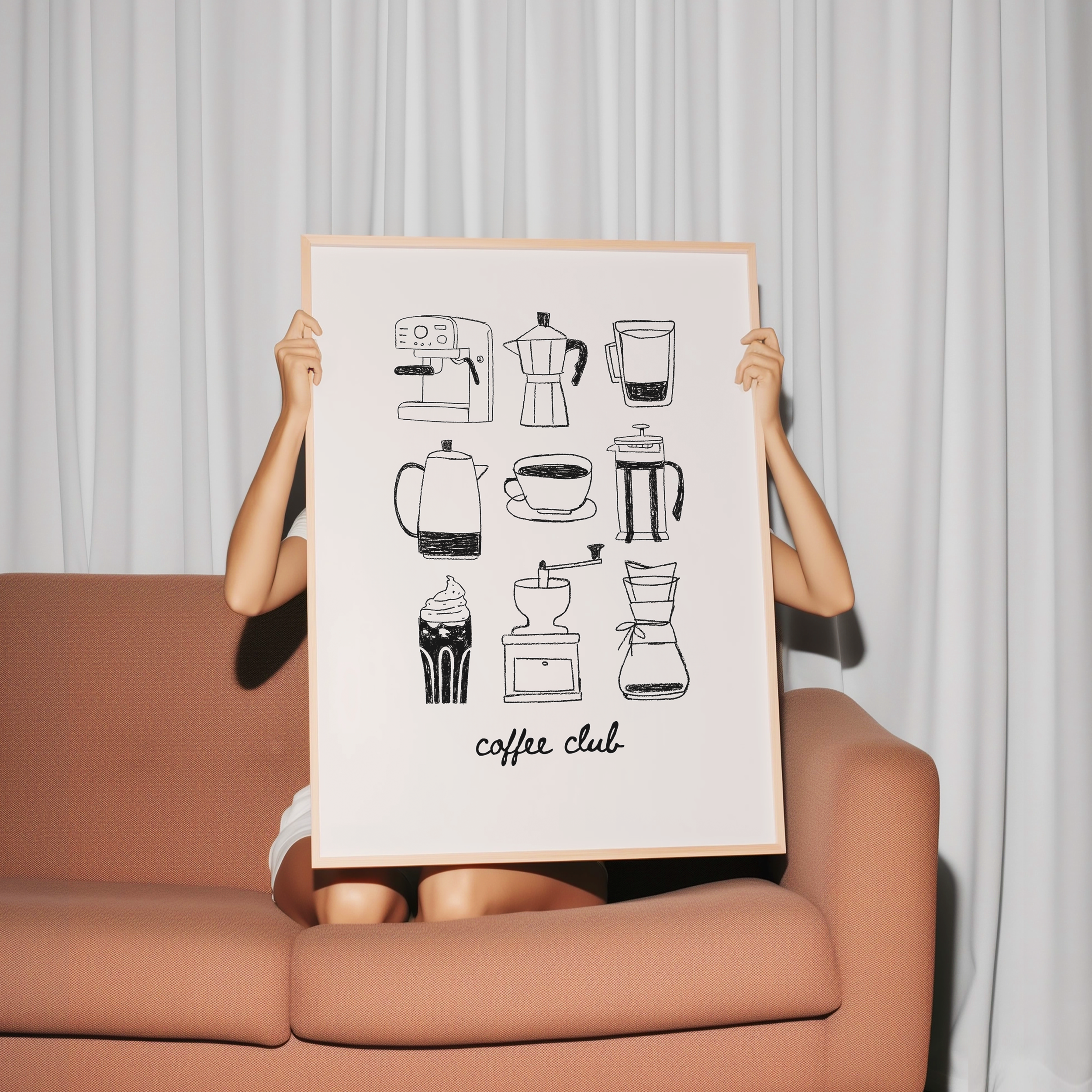 A person is sitting on a couch holding up a framed print with various coffee-related illustrations, including coffee machines, mugs, and other coffee-related items.