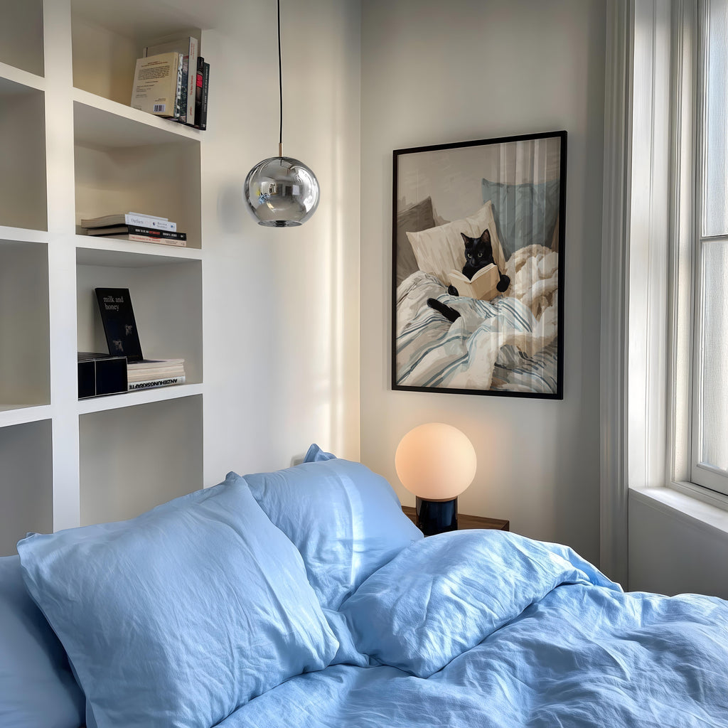 a cozy bedroom with a large bed, a framed picture of a cat on the wall, and a lamp on a nightstand.