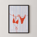 A framed illustration of a red bikini top and a red bikini bottom hanging on a clothesline.