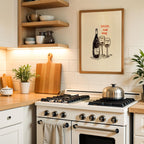 a kitchen with a white stove, wooden cutting board, and various kitchen accessories such as bowls, cups, and a potted plant. Above the stove, there is a framed illustration of wine glasses and a bottle, accompanied by the text "GOSSIP, AND WINE".