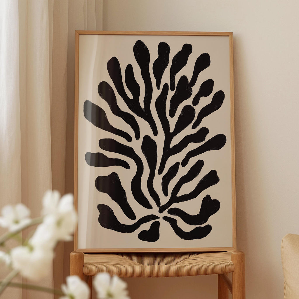 a framed abstract artwork with a black and white design, displayed on a wooden chair against a white wall.