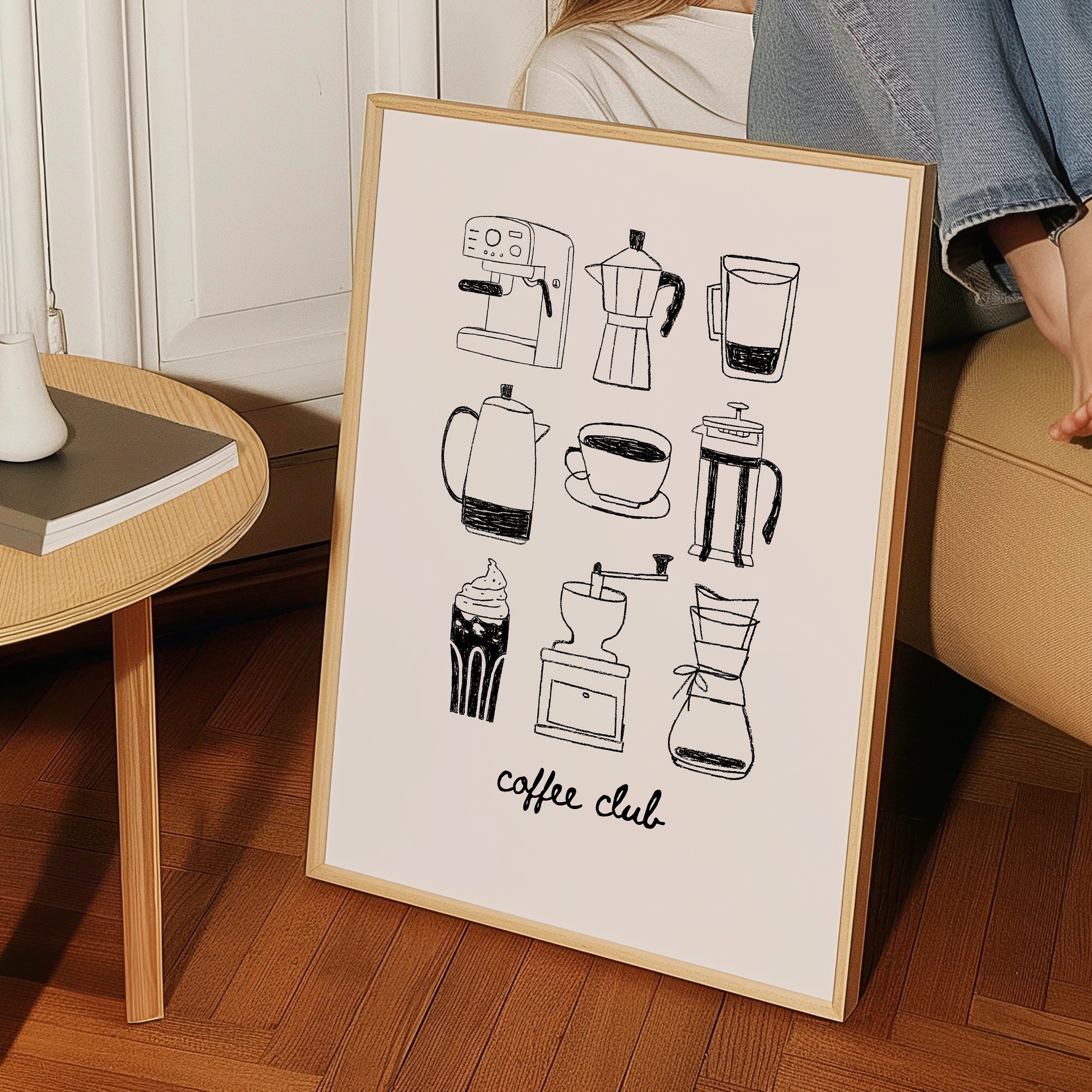 A framed poster with various coffee-related icons and text, including a coffee maker, coffee cup, and other coffee-related items, is displayed on a wooden floor next to a table.