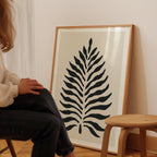 A person is sitting on a chair in front of a large framed print of a stylized leaf design.