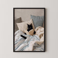A black cat is lying on a bed, reading a book with its paws on the pages.