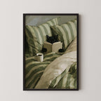 A black cat is lying in bed, reading a book while holding a cup of coffee.
