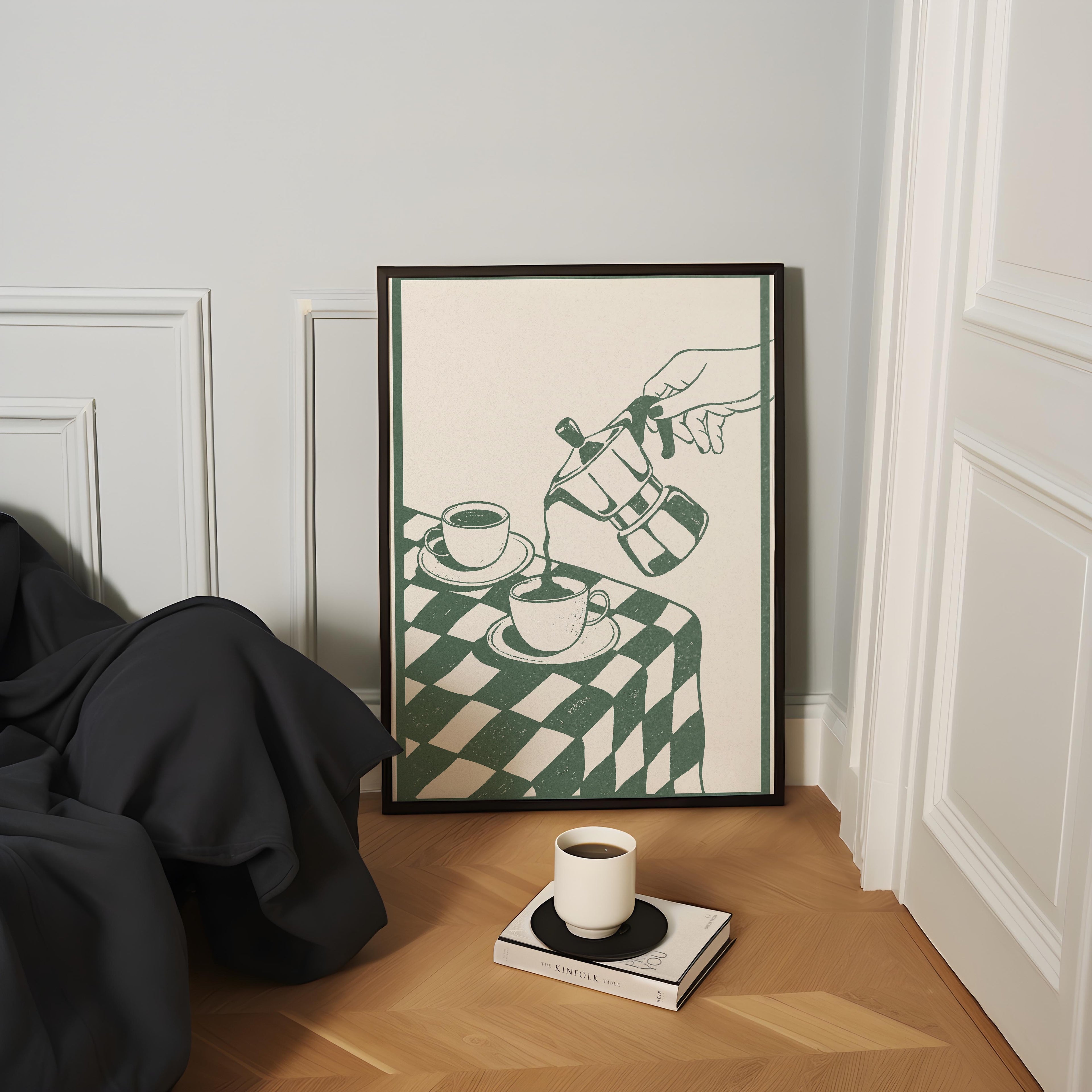 a cozy corner with a framed illustration of a hand pouring coffee into two cups, a white mug, and a book on a wooden floor.