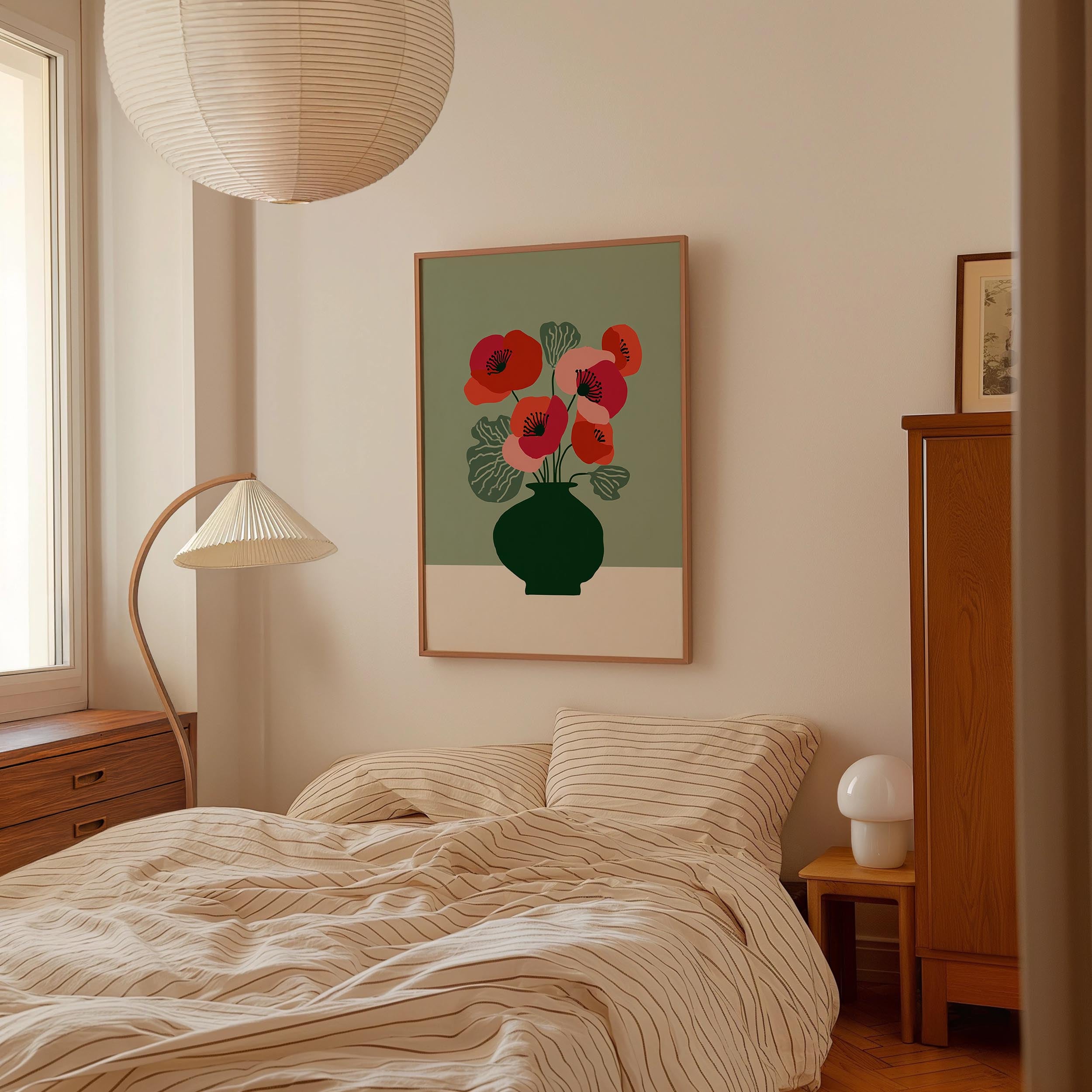a cozy bedroom with a bed, a lamp, and a framed artwork featuring a vase with red flowers.