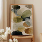 a wooden chair with a framed abstract painting hanging on it, placed in front of a window with white curtains.
