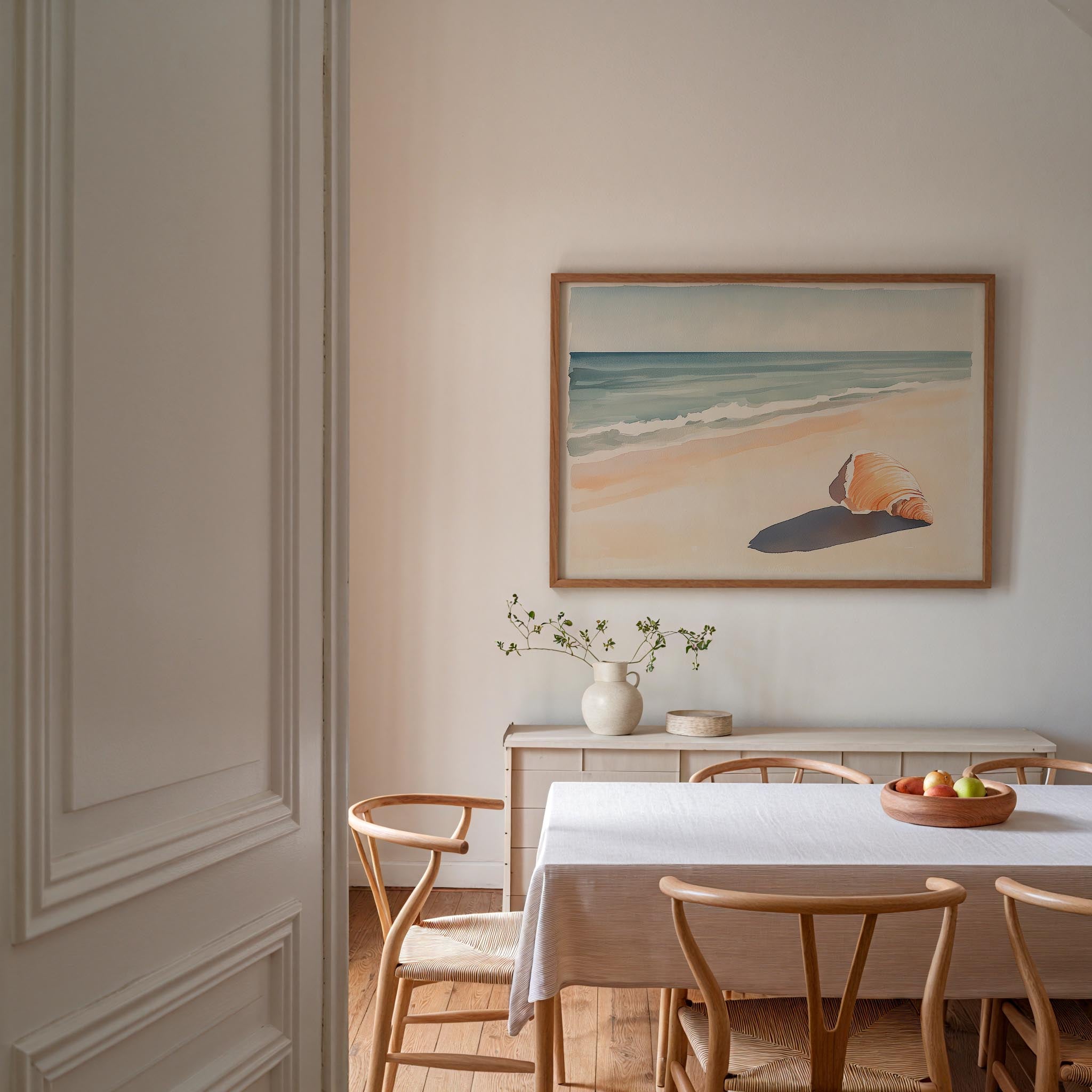 a serene dining room with a white table and chairs, a framed painting of a beach scene, and a vase of flowers on the table.
