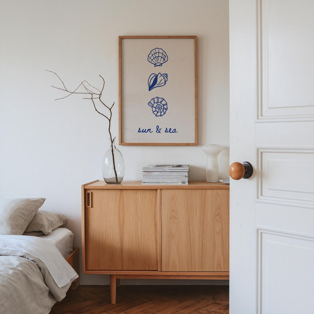 a bedroom with a wooden dresser, a framed poster of seashells, a vase with branches, and a stack of books.