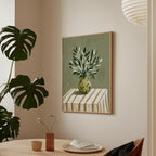 a framed painting of a vase with green leaves on a table, accompanied by a small vase with flowers and a plate of food, all set against a backdrop of a white wall with a potted plant and a hanging lamp.
